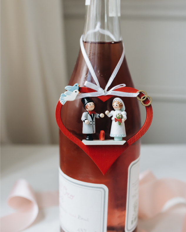 Bottle of rose wine with an original Käthe heart ornament with a bride a groom hanging around the neck of the bottle