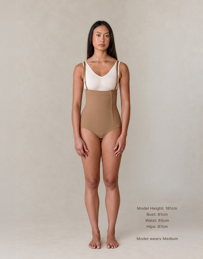 Model wearing the Medium Aesetica latte compression bodysuit with under-bust high waist, brief coverage and adjustable suspenders