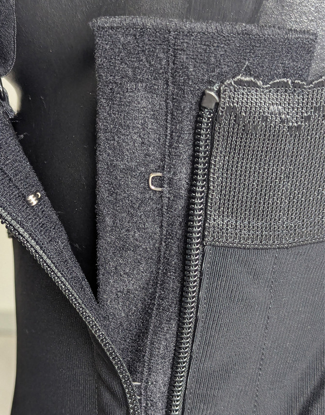 Close-up of the Aesetica compression girdle side closure showing the zip and concealed internal hook fastening for a secure post-operative fit.