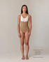 Model wearing the Medium Aesetica latte compression bodysuit with under-bust high waist, brief coverage and adjustable suspenders