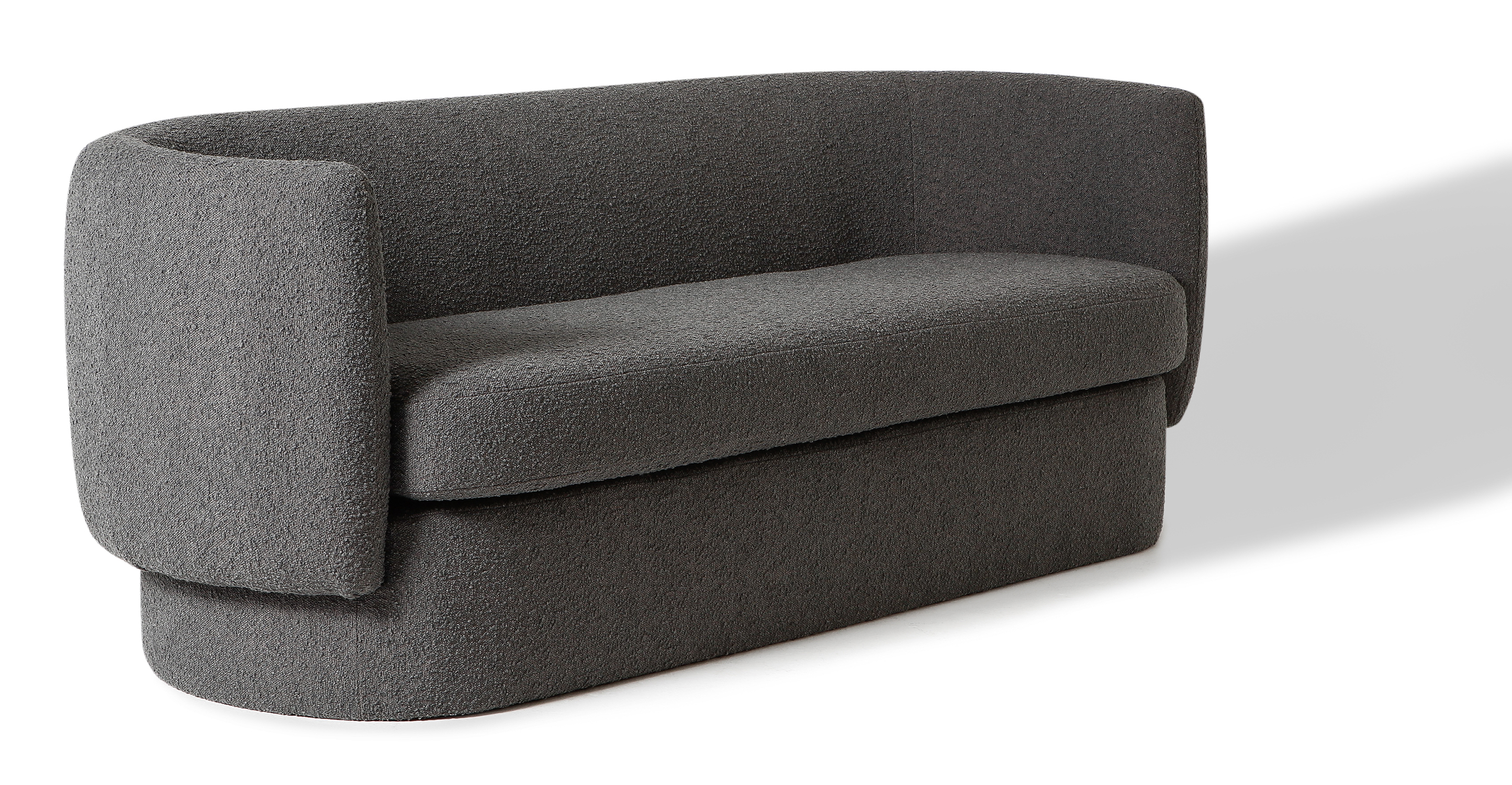 The Swagger sofa is a curved sofa, fully upholstered in gray Gris bouclé fabric. The backrest and wrap-around arms are continuous, forming a semicircle. The seat cushion is removable and is zippered at the back. The base is also fully upholstered. The vibe is bold, modern, and designed to be the focus of a room. 