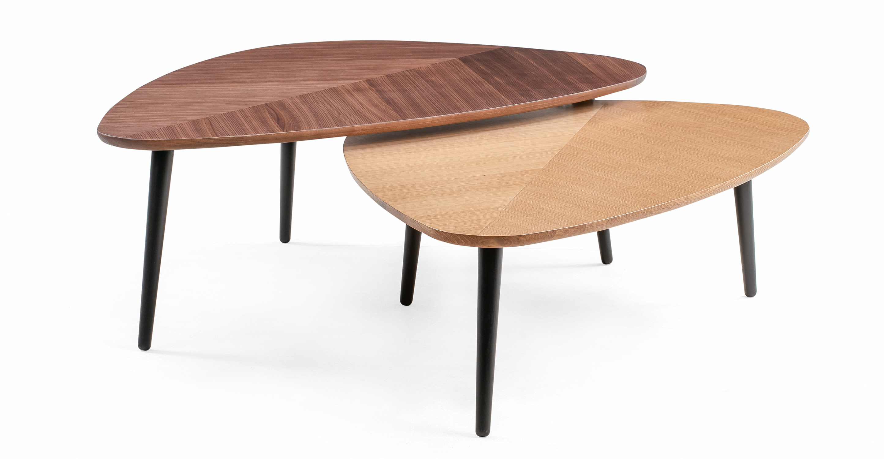 The leaf coffee table has three black wooden Wegner style legs. The table is wider at the back and then narrows towards the front taking on the shape of a leaf. The wood grain pattern meets on the middle of the table and moves outward toward the edge of the table, mimicking a leaf pattern. This set can be nested together as one table is taller than the other or used separately. On table is oak and the other is walnut.