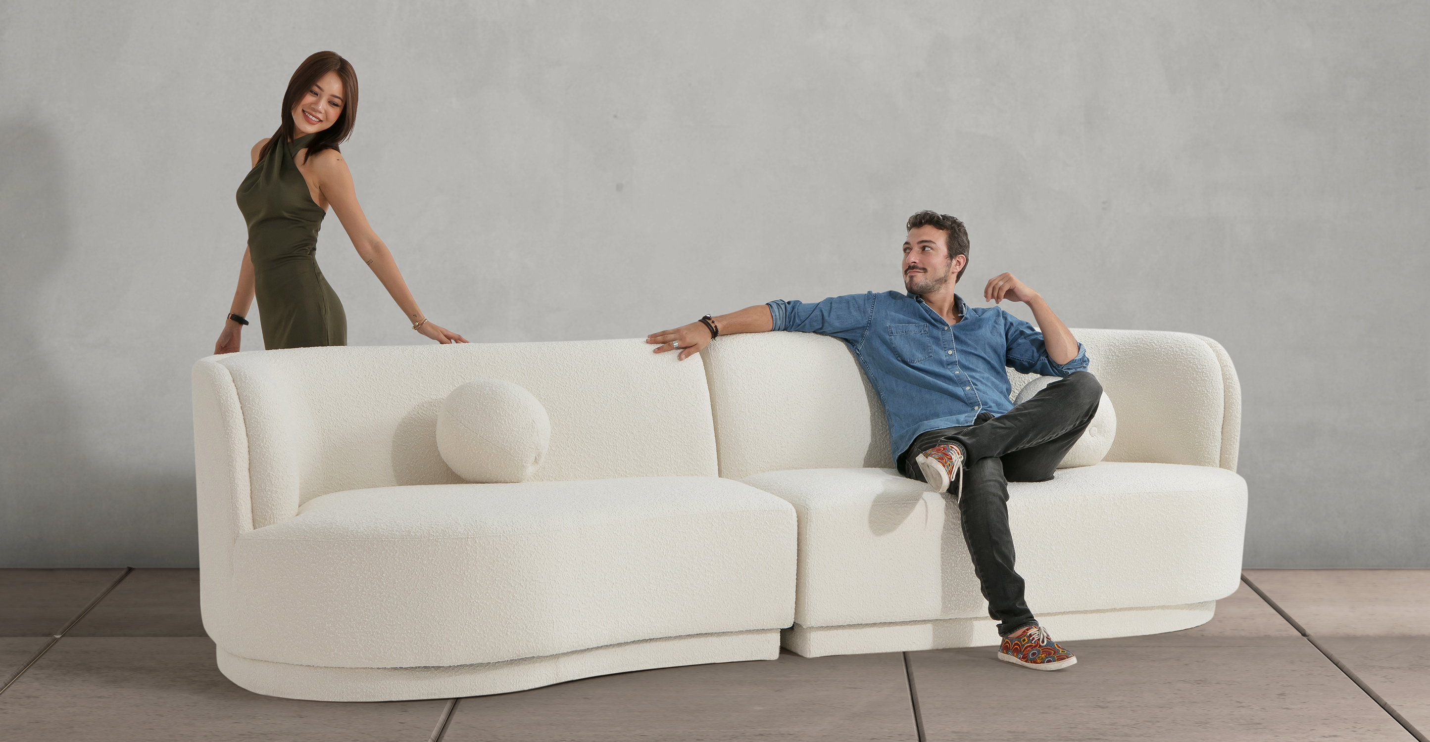 Room scene, showing one person sitting comfortably on the Decorah West 2-pc sofa in Blanc bouclé fabric, while another person stands behind it.