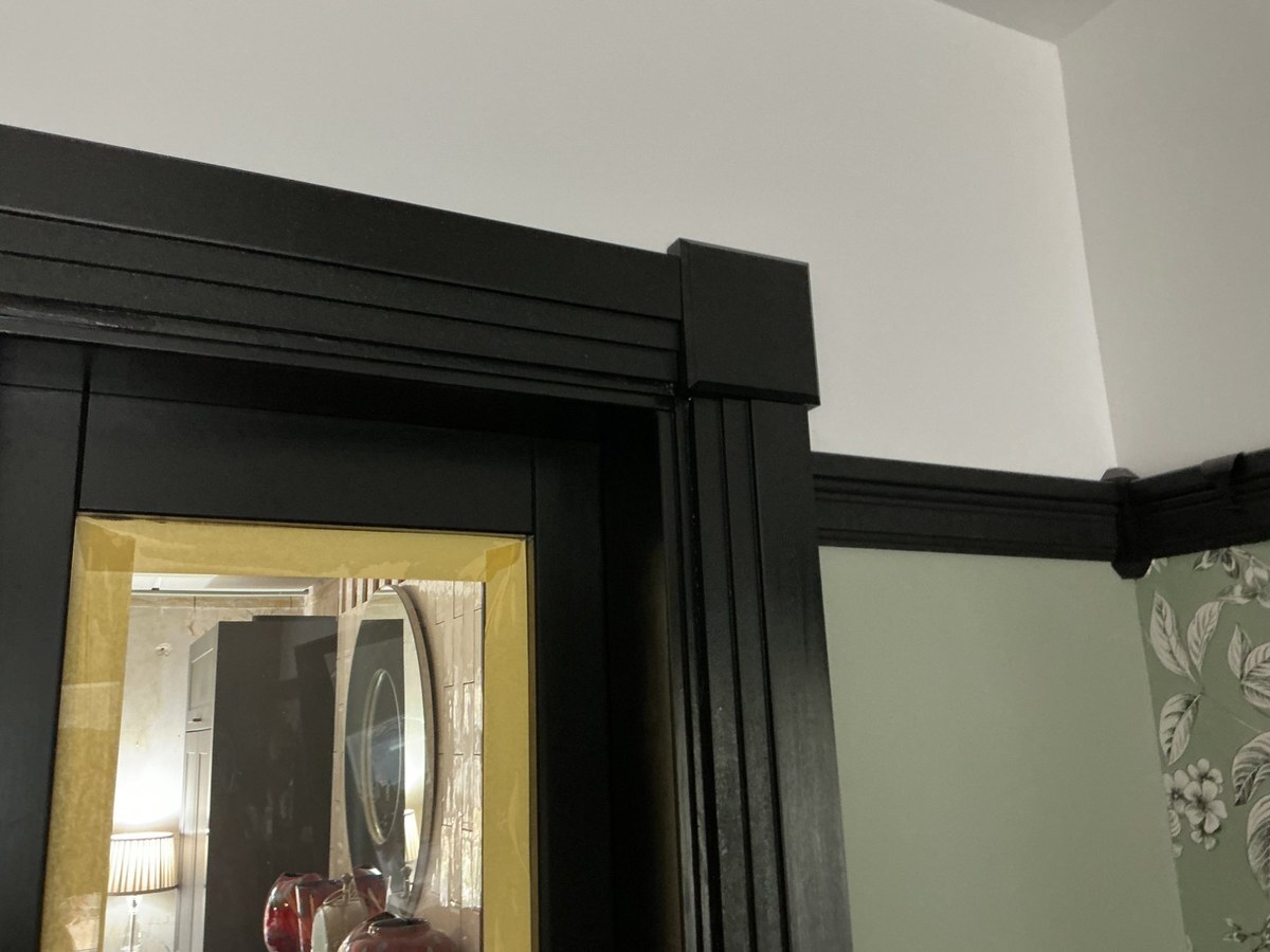 Black Stepped 1 architrave with rosette block and picture rail painted in black against light walls and botanical wallpaper