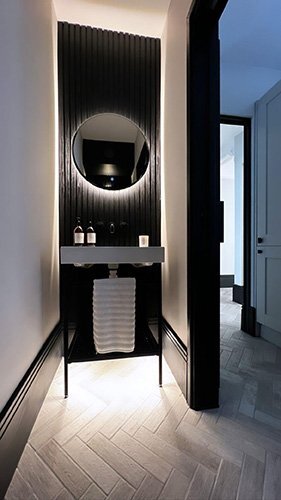 Black fluted wall panel in a modern bathroom with herringbone floor tiles and backlit mirror