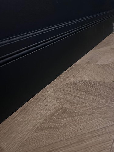 Black moulded skirting board showing profile detail against herringbone oak flooring