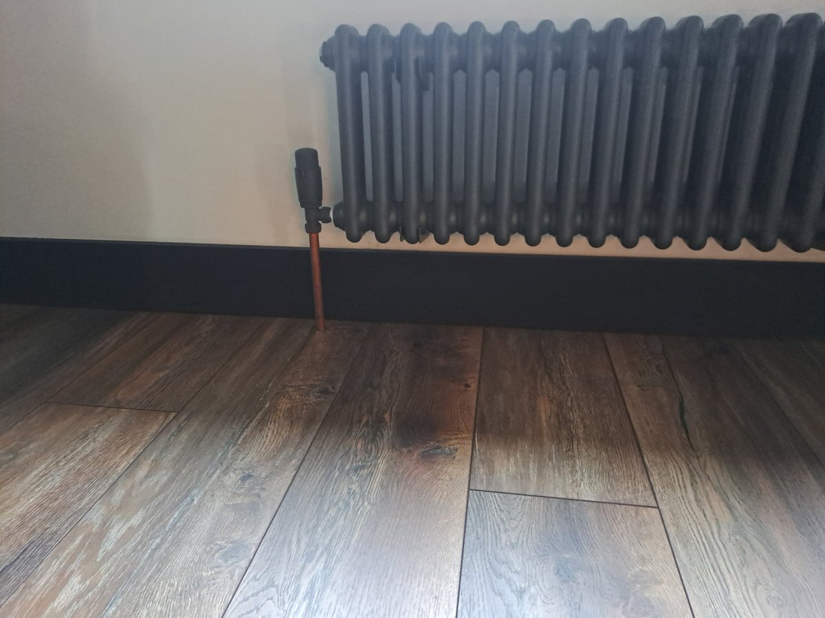 Black skirting board beneath a column radiator on wood effect flooring