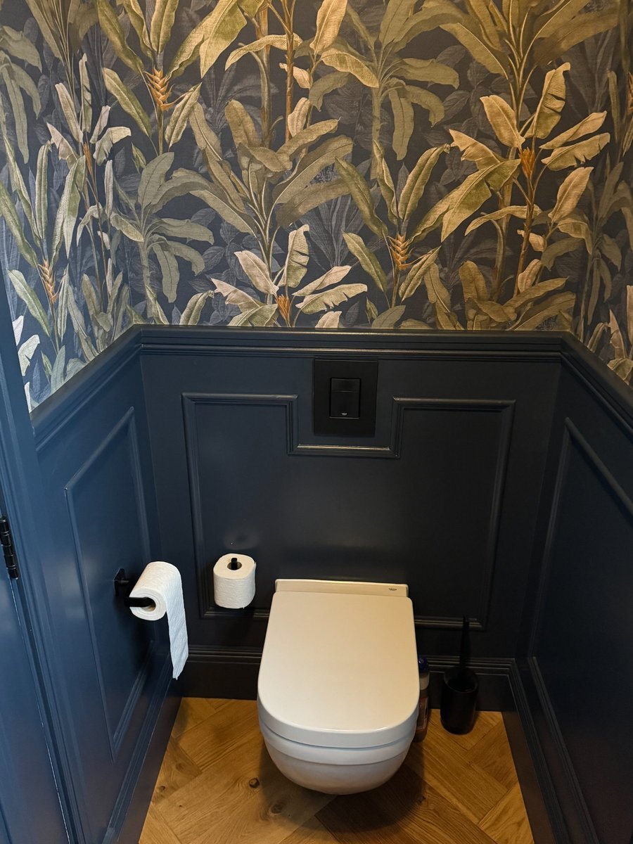 Dark wall panelling in a cloakroom paired with botanical wallpaper above the dado line