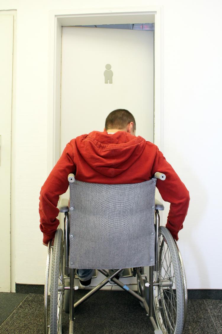 Man in wheelchair demonstrating the challenges of accessing doors that don't meet accessibility requirements