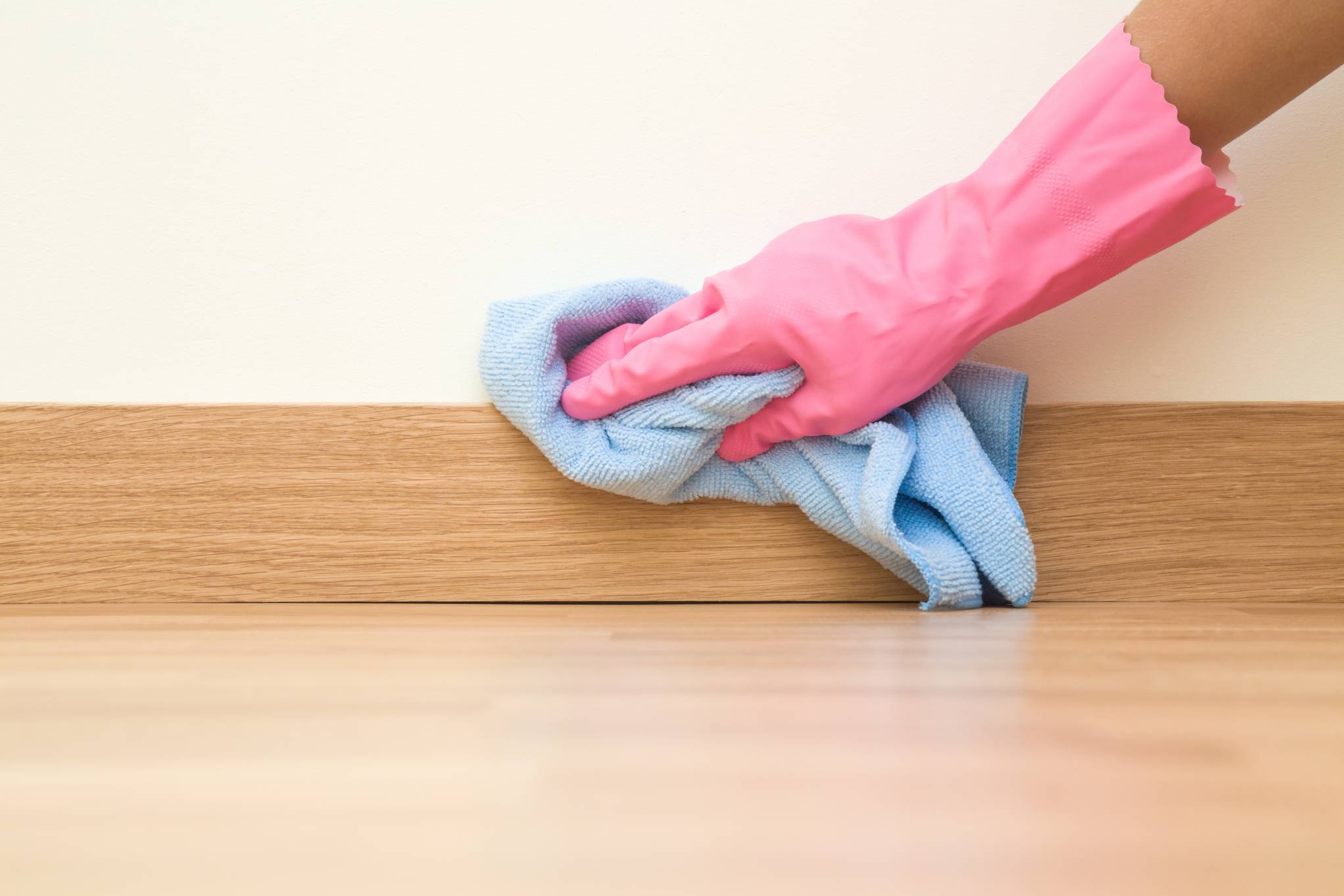 Pink-gloved hand using a blue microfiber cloth to clean an oak skirting board