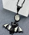black bat pendant with black and white sectioned wings, on a black chain with synthetic round moonstone accent
