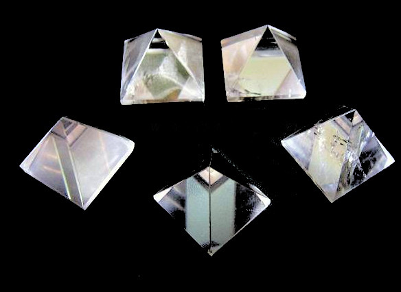 five clear quartz stone pyramids on a black background