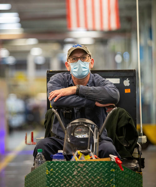 A man wearing a facemask sits with his arms crossed on a motorized cart.