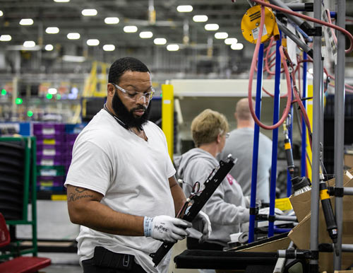 A Black man inspects a part while working in a GE warehouse.