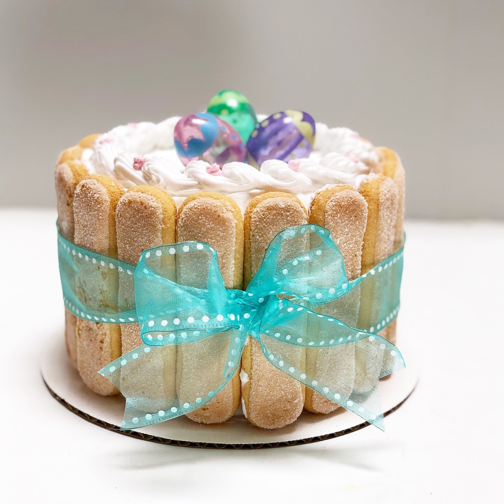Cathy's classic holiday design for Easter. Featuring lady fingers around the cake wrapped like a package with a bow and non-edible Easter egg figurines on top.