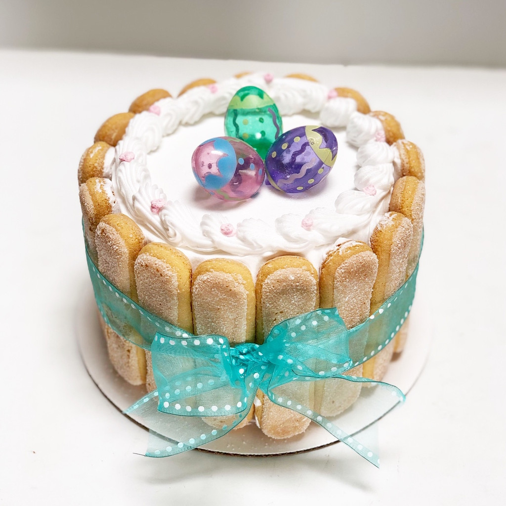 Cathy's classic holiday design for Easter. Featuring lady fingers around the cake wrapped like a package with a bow and non-edible Easter egg figurines on to