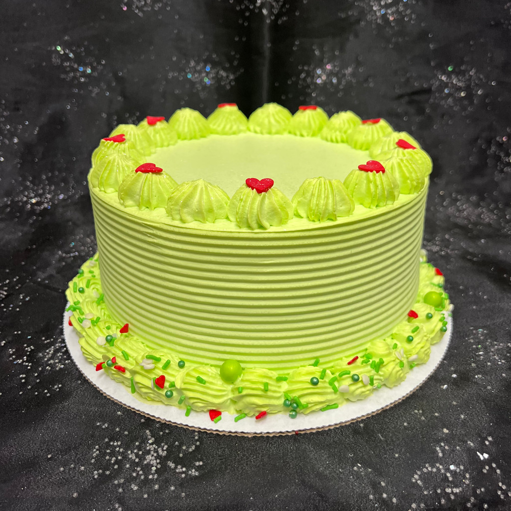 Green tinted Italian whipped cream frosting, raked border on sides, traditional border on bottom with assorted red + green sprinkles, who-hills on top with confetti hearts too sizes too small. 