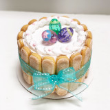 Cathy's classic holiday design for Easter. Featuring lady fingers around the cake wrapped like a package with a bow and non-edible Easter egg figurines on to