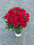 Two dozen red roses presented with seasonal foliage in a complimentary vase. 