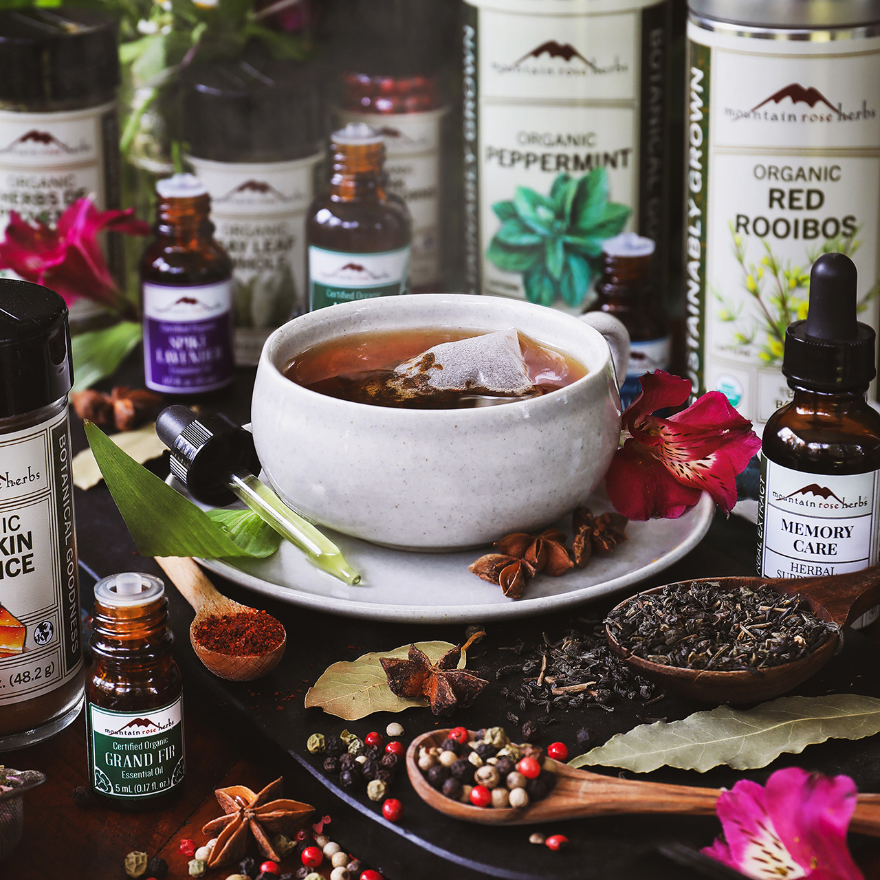 Mug of tea surrounded by dried herbs and spices and Mountain Rose Herbs products. 