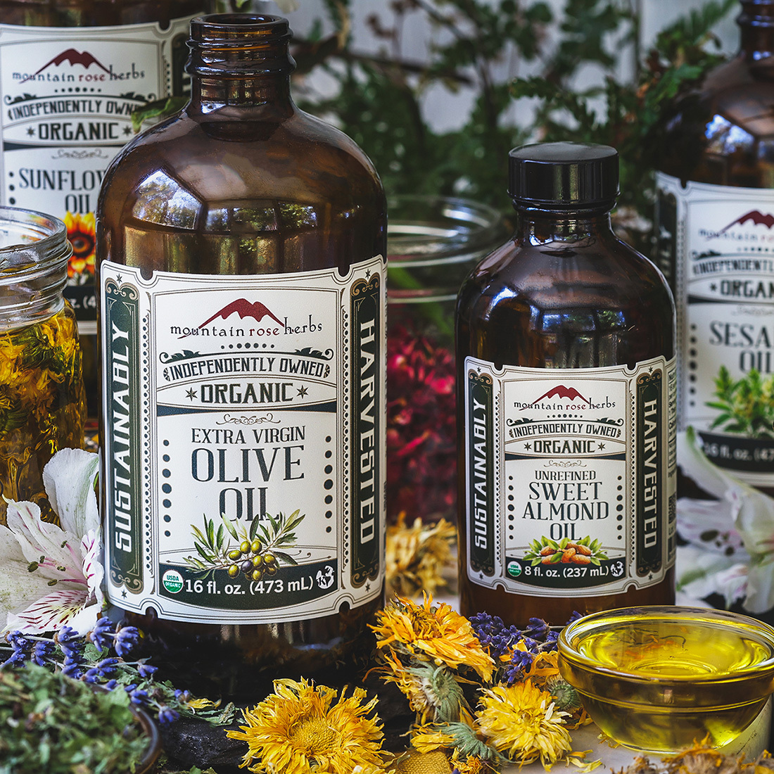 Bottles of Mountain Rose Herbs' New Culinary Oil s surrounded by dried and fresh flowers. 