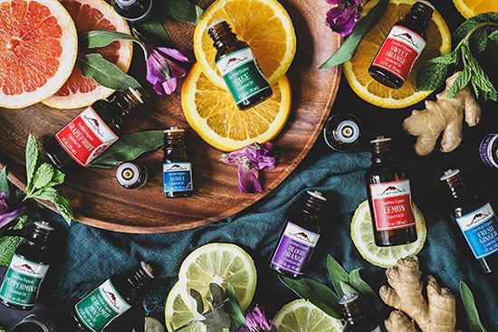 Bottles of essential oils surrounded by fresh flowers and citrus slices. 