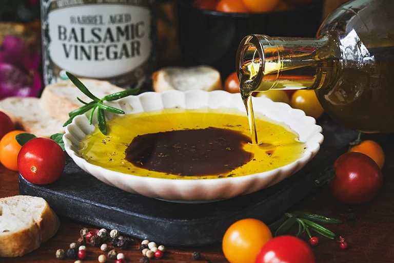 Bowl of oil and balsamic vinegar in a plate surrounded by fresh tomatoes and spices. 