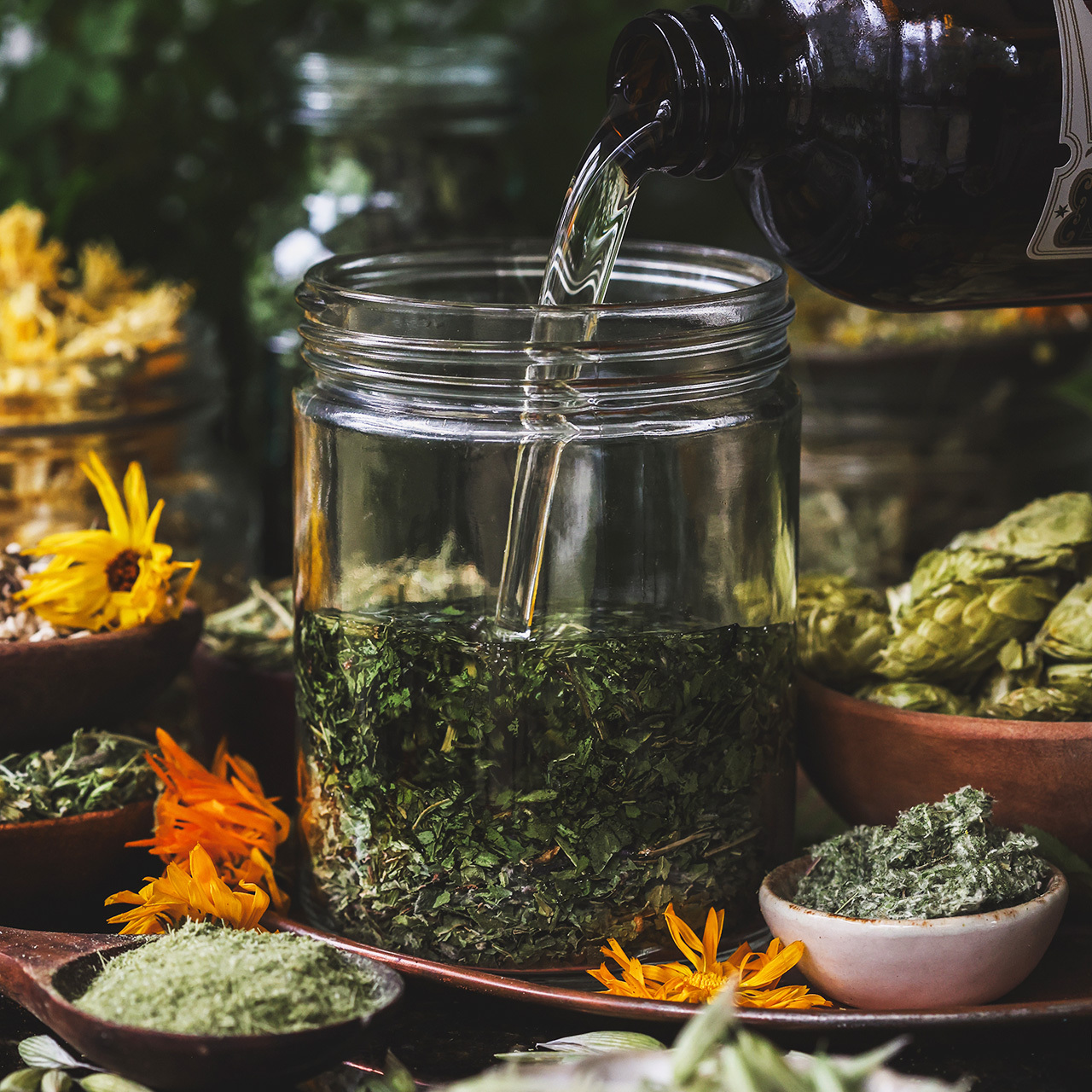 Jar half way filled with herbs and oil being poured on top. 