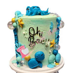 The Cake Mixer Under the Sea Baby Shower Cake, decorated with a cute blue octopus figure on top, sea-themed decorations such as starfish, shells, and seaweed, in pink and blue colors, for a baby shower celebration.