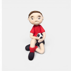 Handmade soccer gumpaste figurine cake topper featuring a sitting football player holding a soccer ball for sports-themed birthday cakes.