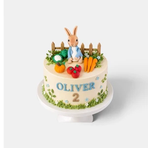 Deluxe Peter Rabbit cake with handmade blue jacket bunny, vegetable garden, flowers, fence and personalised name and age.