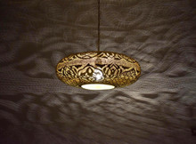 Moroccan style brass lantern pendant light illuminating a dining table, with artisan cutout designs that create an exotic glow.