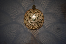 Moroccan brass hanging bedside light fixture with intricate cutouts, casting decorative shadows in bedroom spaces.