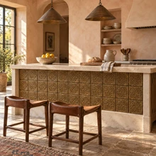 Woven Star Knot Celtic knot tiles in hand-embossed brass, set into the front of a plaster kitchen island with leather stools