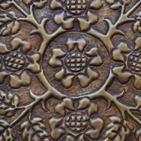 Close-up of the hand-embossed Tudor rose relief showing the hand-punched ground and darker patina in the recesses