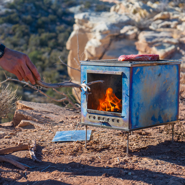 Camp cooking on Seek Outside stove grill top with fire roaring through the glass door.