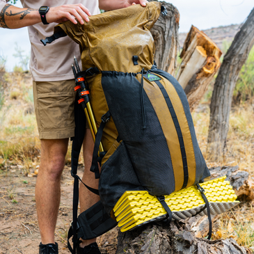 person adjusts the roll-top closure of Divide backpack, 38" unrolled height