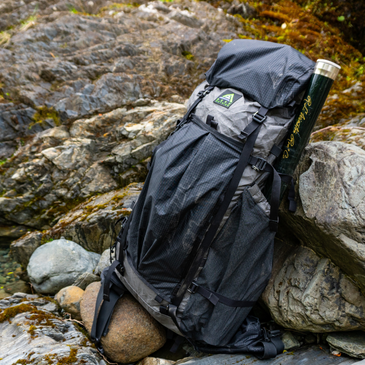 a gray Ultra200 Goshawk backpack leaning against a boulder on rocky ground