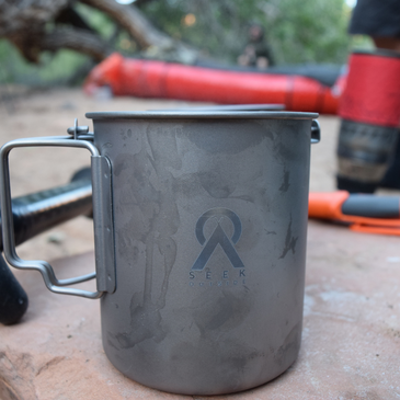 a titanium mug sitting on a rock in a campsite