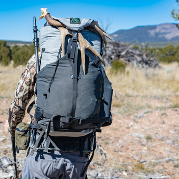 a man walking across rocky ground wears a Revo suspension frame with a Silverton backpack connected to it, there are deer antlers in the backpack