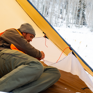 hunter laying inside a cimarron tent, installing the floor liner system to the side walls of the tent