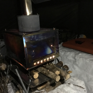 wood piled under a titanium stove inside a Courthouse tent
