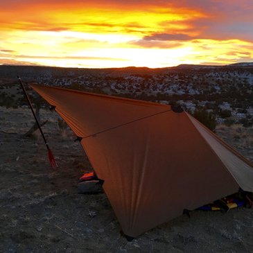 DST tarp set up up with boat oar, snow covered bushes and sunset in the background