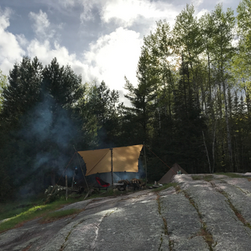 a campsite with a tarp set up, smoke raising from a fire, surrounded my trees and a cloudy sky
