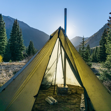 Sun shining through 30D silnylon canopy of 8 person tipi tent with stove and stovepipe inside 