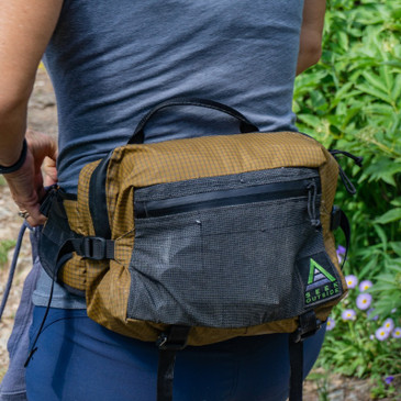 Day hiker carrying Seek Outside Mesa hip pack, new 2-inch waist strap visible, load lifters bringing pack close to back for comfort