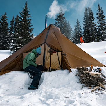 12 person tipi tent staked in deep snow, fire burning inside and gear hanging to dry inside 260 square foot interior