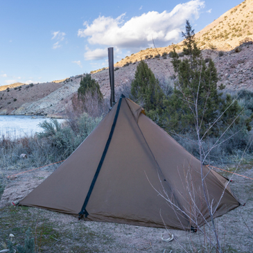 Riverside camp with Seek Outside Cimarron shelter, stove pipe visible, and mountain stream in background