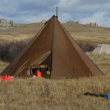16 person tipi hot tent in backcountry hunting camp with rifles, packs, and cots inside