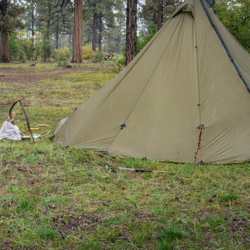 backcountry hunting camp with 8 person tipi tent in steady rain, guyout loops tightened to steepen walls for weather resistance
